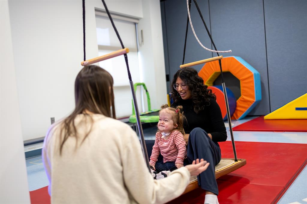 Women holding a small girl on a large swing in treatment room